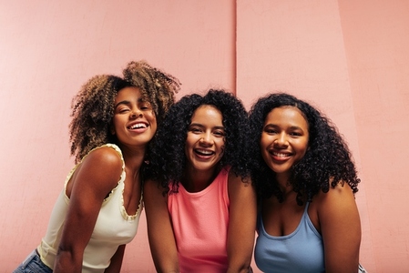 Three happy girls with curly hair  Smiling females wearing colorful t shirts looking at the camera