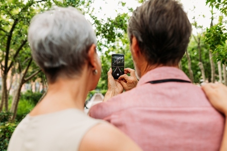 Back view of a senior couple taking a street photo while walking in the park
