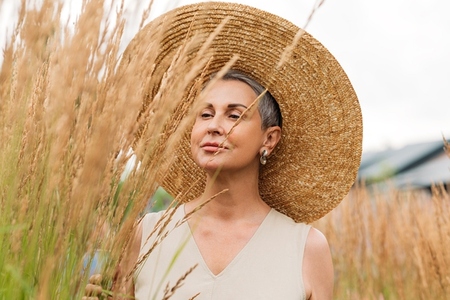 Senior female with short grey hair wearing a straw hat looking at wheat