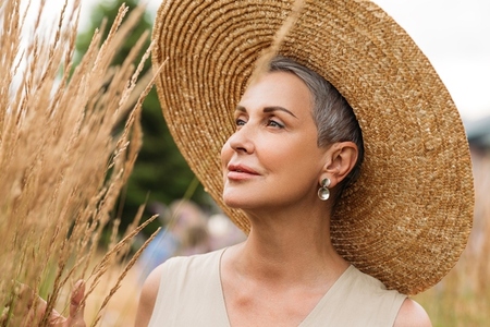 Close up mature female with short grey hair wearing a straw hat looking at wheat