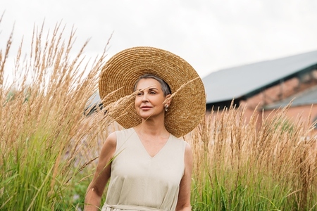 Aged female in a straw hat walking on a wheat field