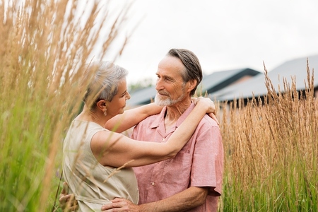 Mature couple in casuals looking at each other and hugging while standing on a wheat field