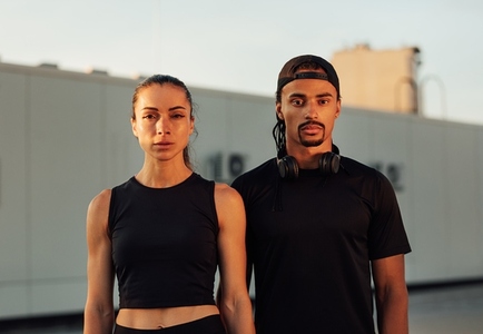 Portrait of two athletes in black sportswear standing together  Young athletes relaxing on the roof at sunset