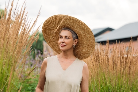 Aged woman with grey hair wearing a big straw hat walking on the wheat field