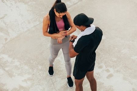 Shot from above on two athletes checking their smartwatch after training  Fitness couple adjusting fitness trackers