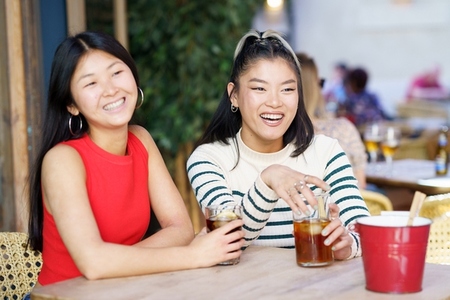 Positive Asian girls resting in cafe with drinks