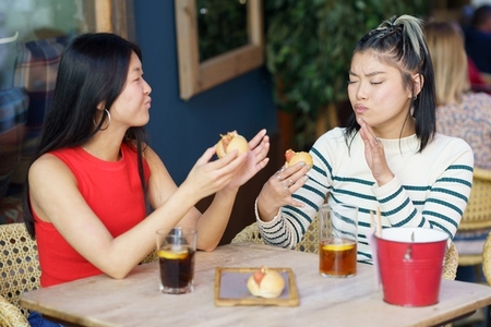 Satisfied Asian women eating tasty meal in cafe together