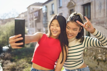 Positive Asian female tourists shooting selfie on cellphone