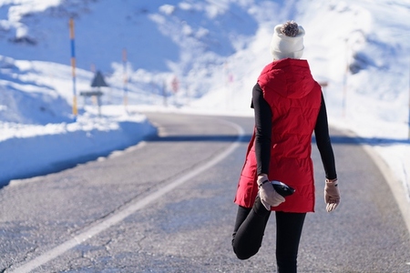 Unrecognizable woman in outerwear stretching on road
