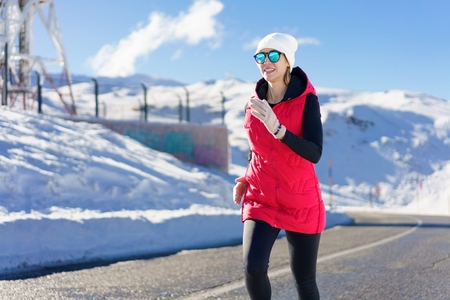 Happy young female in warm clothes and cap running on road