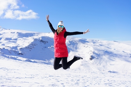 Carefree young woman jumping with raised arms on snow terrain