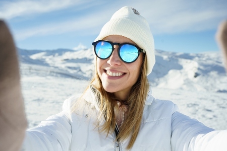Cheerful woman in sunglasses taking selfie in snowy place