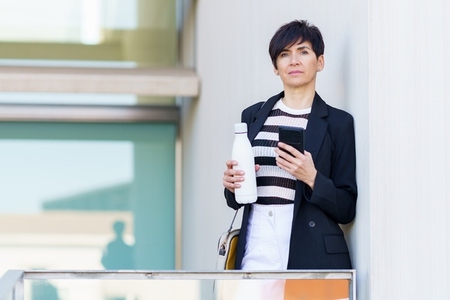 Serious adult female with bottle of milk in hand and using mobile