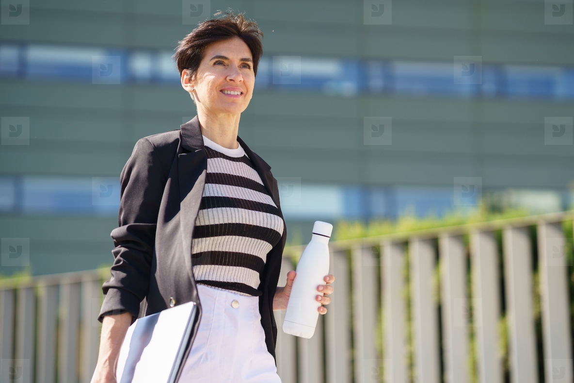 Positive woman with bottle of water to go on street in daytime