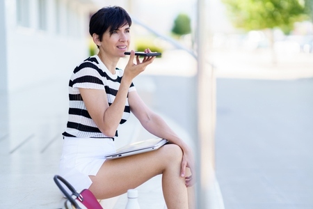 Cheerful woman recording voice message on smartphone