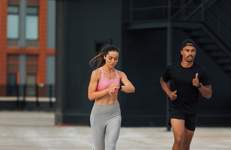 Two athletes sprinting on a rooftop  Young woman checking fitness tracker while running