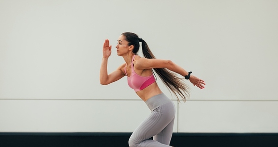 Side view of slim woman with long hair in sportswear running at a wall