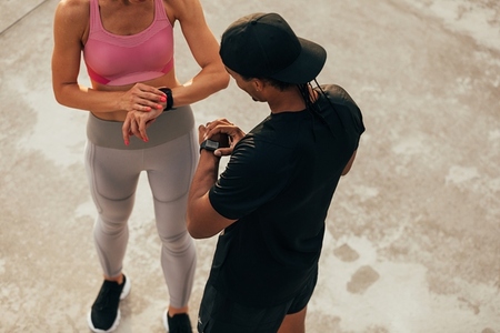 High angle of two people in sportswear checking their smartwatches after training