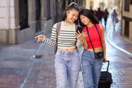 Asian girlfriends traveling together walking on street and browsing smartphone