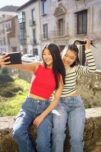 Happy Asian girlfriends taking selfie on bridge