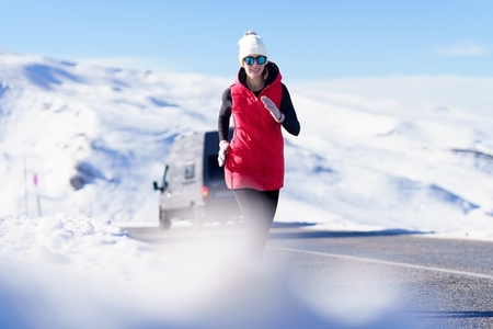 Sportive woman in warm clothes running on road in mountains