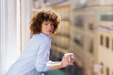 Curly haired female drinking coffee on balcony