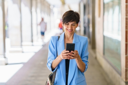 Happy mature woman messaging on smartphone on city street