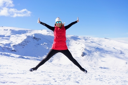 Cheerful woman in warm clothes jumping in air on snow terrain