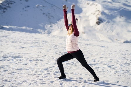 Slim woman stretching in warrior pose over snowy mountains