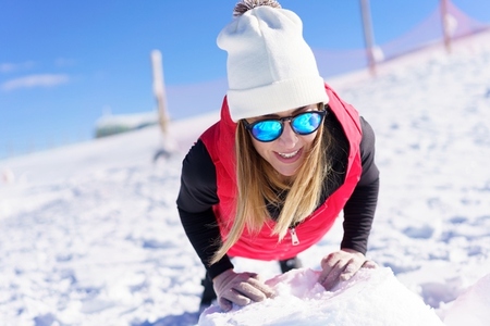 Smiling young woman in beanie wool cap and sunglasses warming up on snow