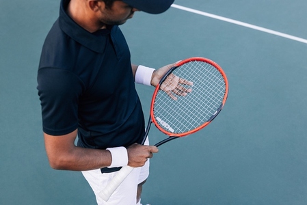 High angle of an unrecognizable male adjusting his tennis racket