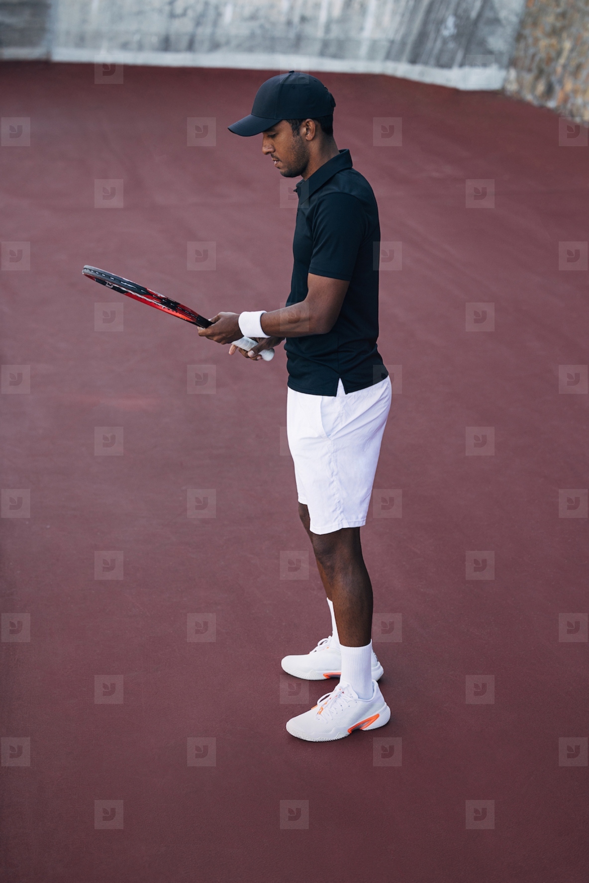 Side view of a male tennis player in sportswear adjusting his racket