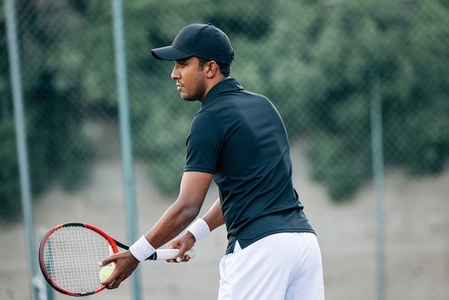 Side view of a professional tennis player holding a racket and ball preparing to serve