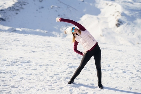 Young woman standing and doing exercise on snow in highlands