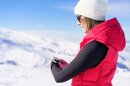 Young woman standing in snowy terrain and checking time