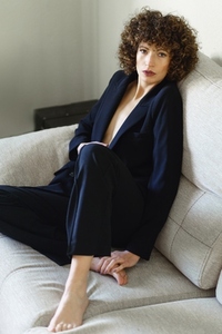 Stylish curly haired woman sitting on sofa wearing black suit