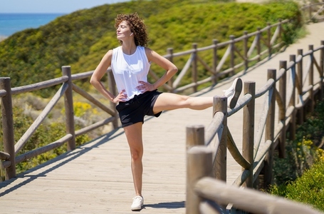 Happy young woman warming up with stretching leg on bridge