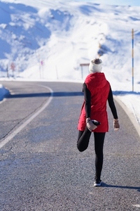 Anonymous sportswoman stretching on winter road