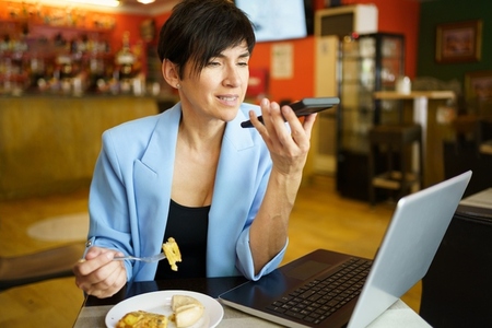 Serious woman recording audio message on smartphone while eating in cafe