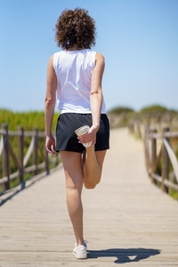 Unrecognizable young woman standing and stretching on wooden bridge