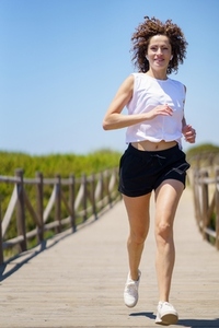 Fit sportswoman jogging along boardwalk on summer day