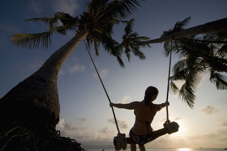 Young woman at sunset on a swing between palm trees Thailand