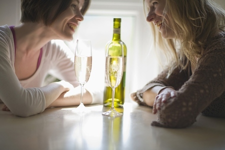 Two young women sitting at table talking laughing and drinking wine