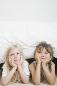Two young girls with chin resting on hands under bed
