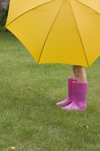 Young girl in pink boots under yellow umbrella