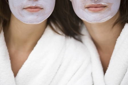 Close up of two young women with mauve beauty mask and white bathrobes