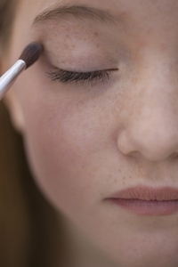 Close up of young woman applying eye make up with eyeshadow brush