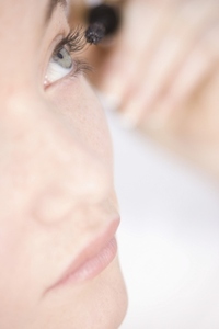 Young woman applying eye make up with mascara brush