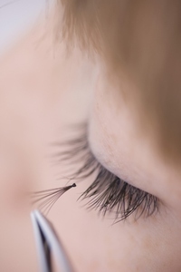 Close up of young woman applying individual eyelash with tweezers