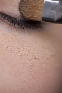 Woman applying eye make up with eyeshadow brush and makeup powder under eye
